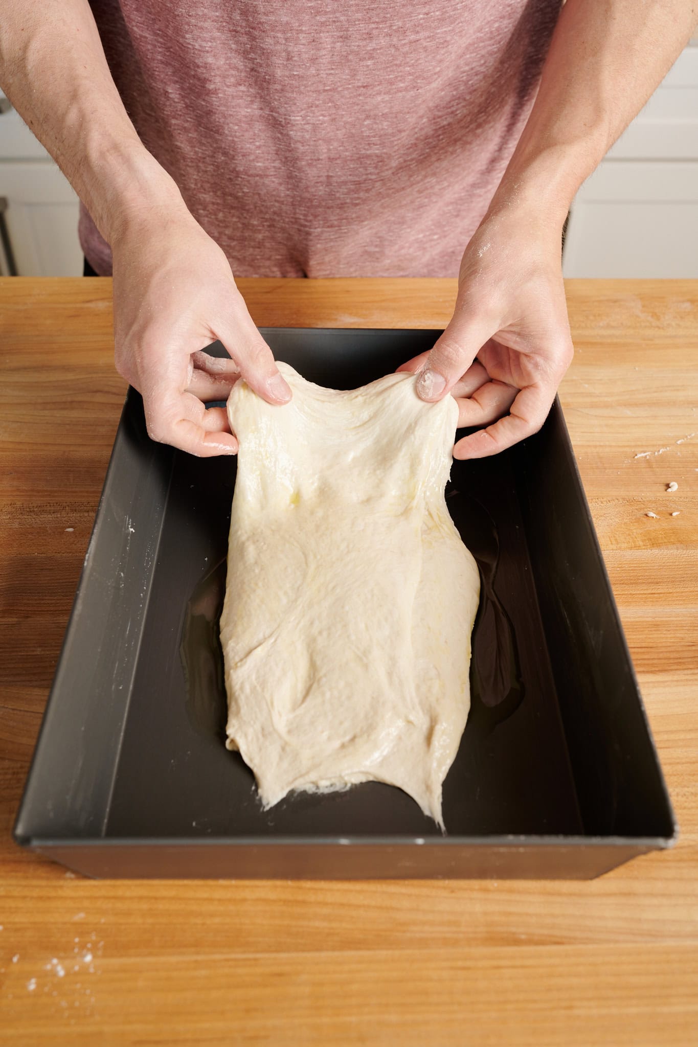 Stretching Detroit-style pizza dough out to fit pan.