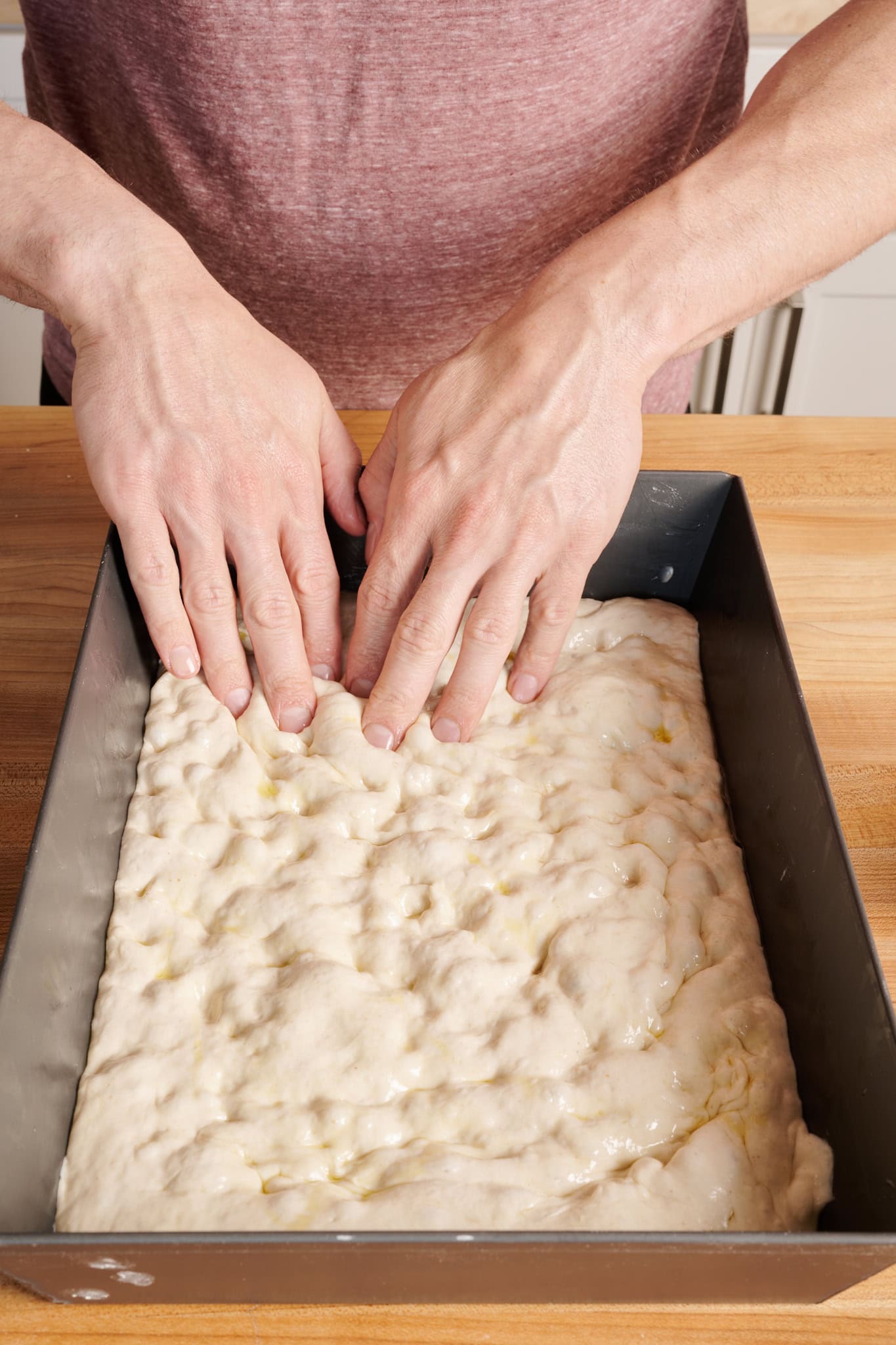 Dimpling Detroit-style pizza dough.